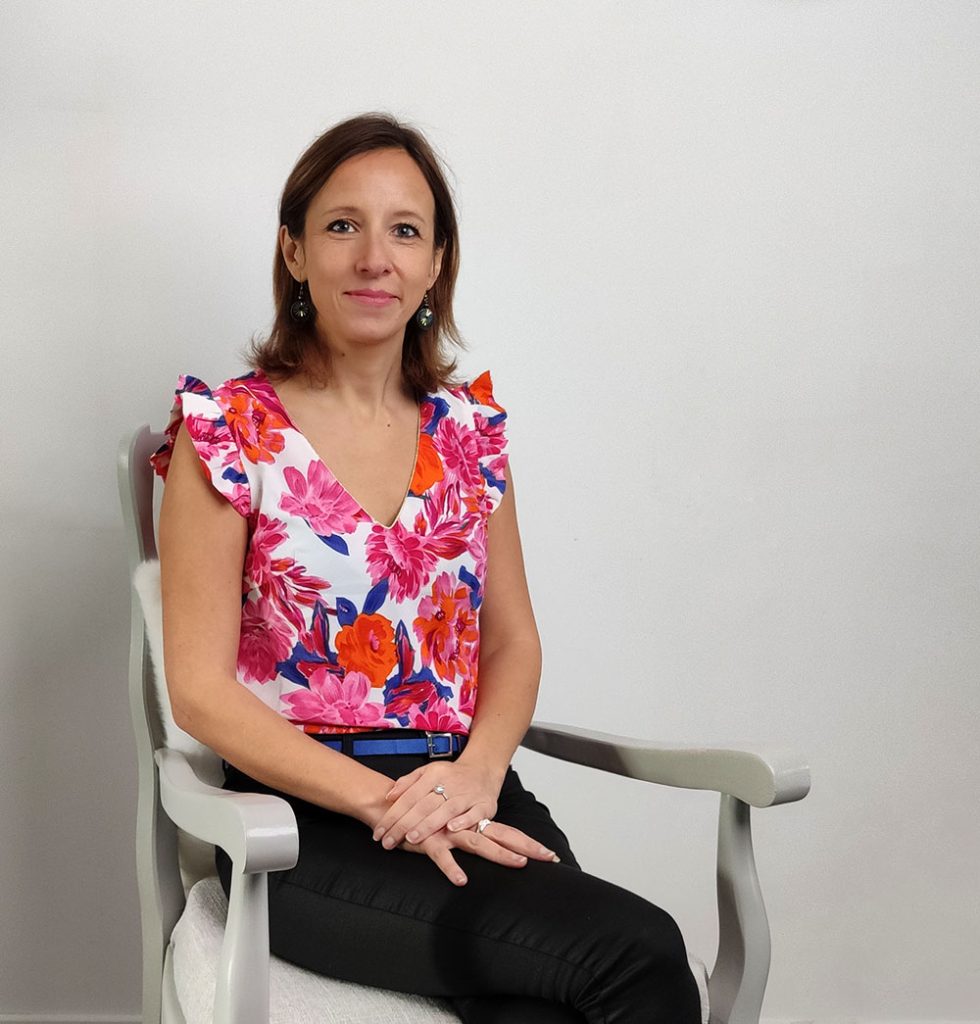 Femme assise dans un fauteuil, portant un haut coloré à fleurs